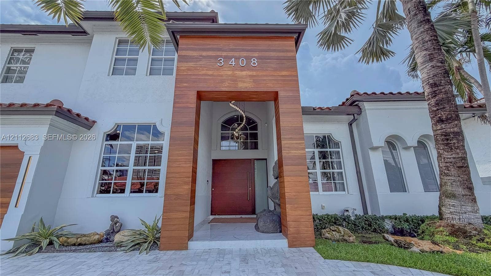 Stucco exterior with a wood-clad entryway, multi-pane arched windows, tile roofing, and stone paver driveway