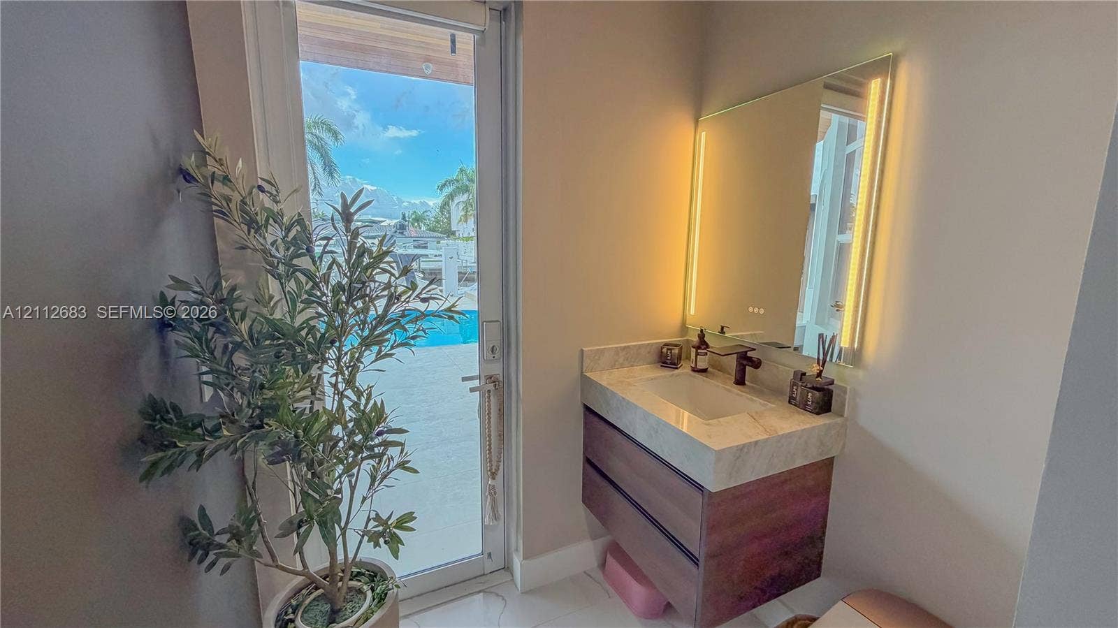 Floating wood-finish vanity with integrated stone-look countertop, rectangular undermount sink, dark-toned wall-mounted faucet, and rectangular back-lit mirror