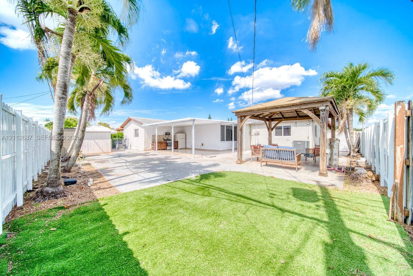 9340 SW 26th Street, Miami, FL 33165 Fenced backyard featuring synthetic turf, a covered concrete patio, a wooden gazebo, and mature palm trees