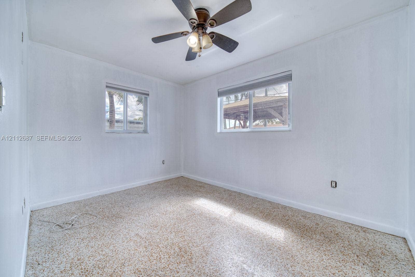 9340 SW 26th Street, Miami, FL 33165 Neutral-toned interior featuring terrazzo flooring, two sliding-sash windows with roller shades, and a ceiling fan with integrated lighting