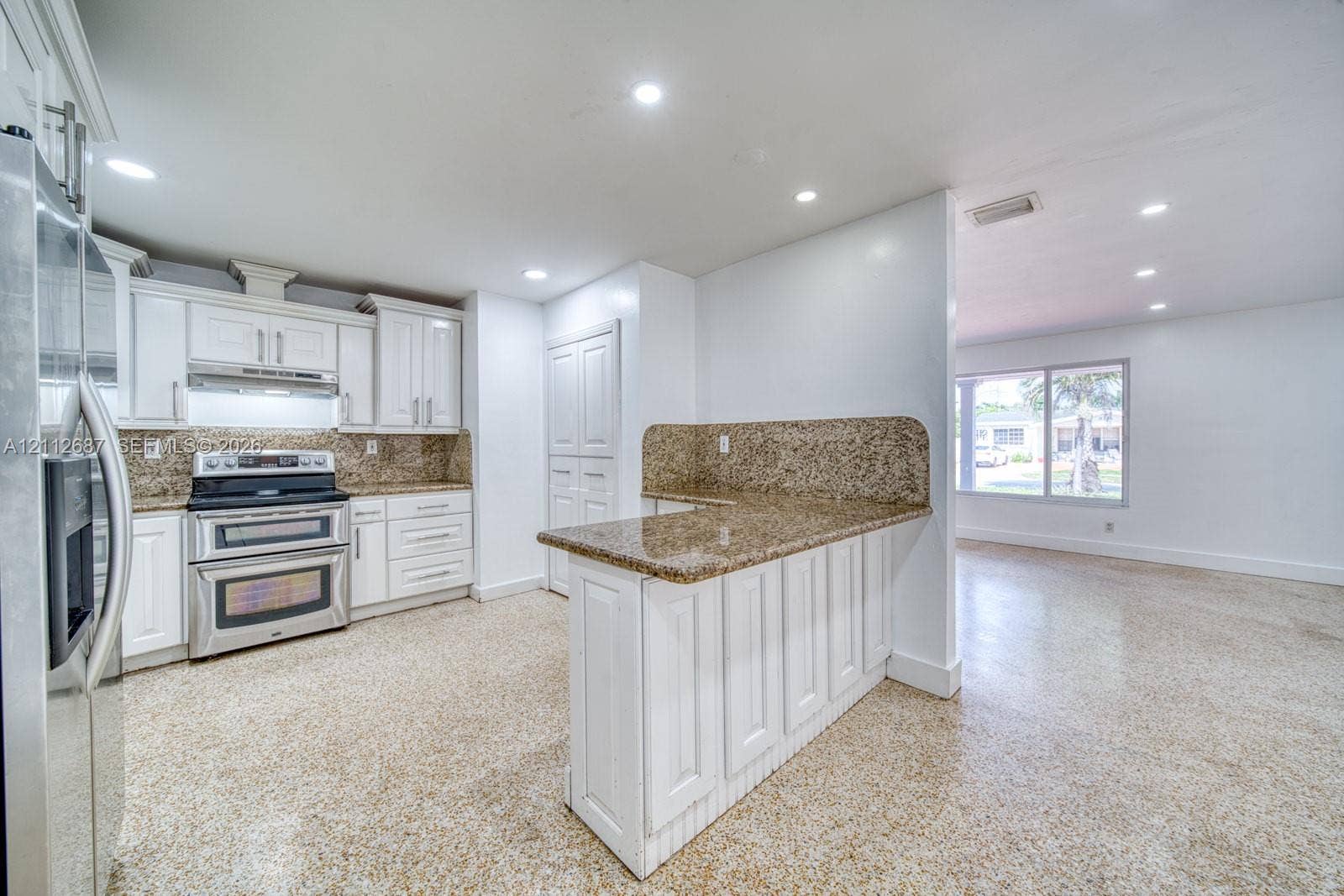 9340 SW 26th Street, Miami, FL 33165 Kitchen featuring white shaker-style cabinetry, stone-surface countertops, stainless steel appliances, a peninsula with bar seating, and polished aggregate flooring