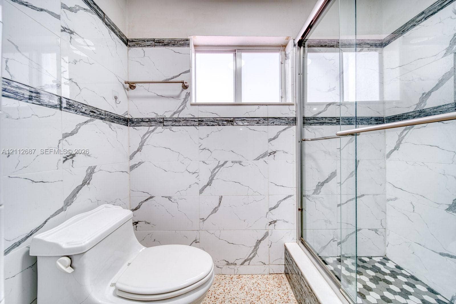 9340 SW 26th Street, Miami, FL 33165 Bathroom featuring floor-to-ceiling white veined wall tile, glass-enclosed shower with hexagonal tile flooring, and a sliding window