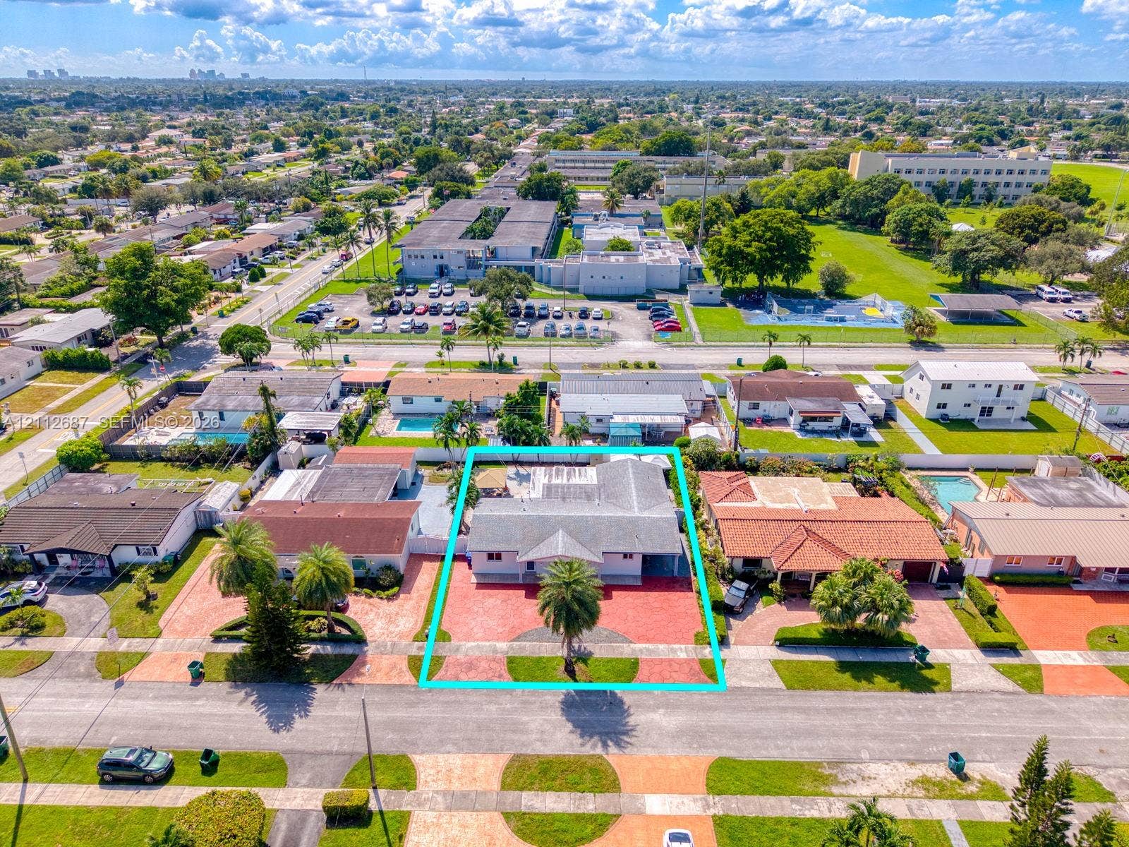 9340 SW 26th Street, Miami, FL 33165 Aerial perspective of a single-story residence featuring a shingled roof, a paved front driveway, a prominent palm tree, and a fenced backyard