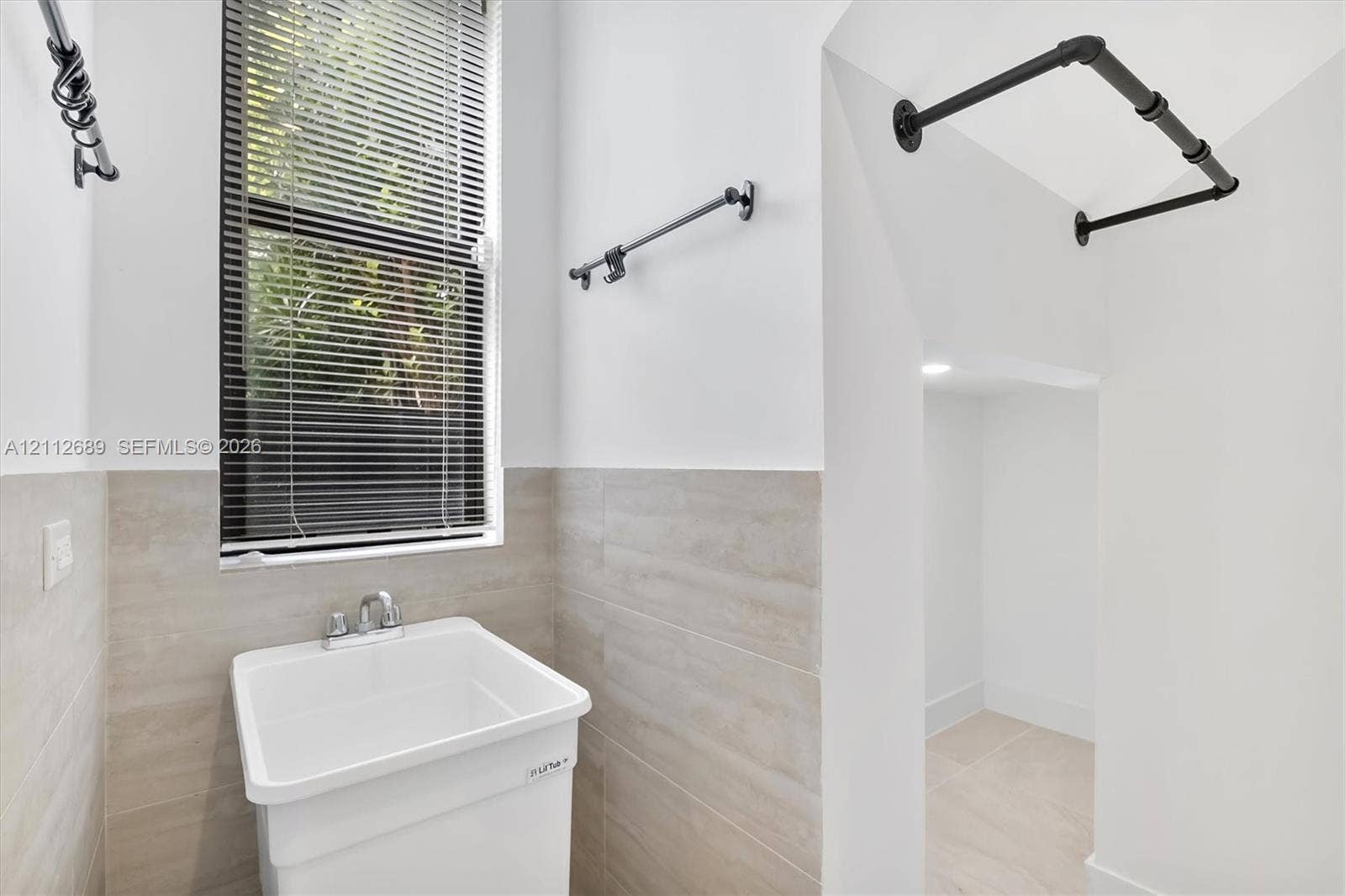 2889 SW 33rd Avenue, #2889, Miami, Miami, FL 33133 Utility space featuring a basin sink with chrome faucet, neutral wall-tile wainscoting, matte black wall-mounted hardware, and an open storage alcove