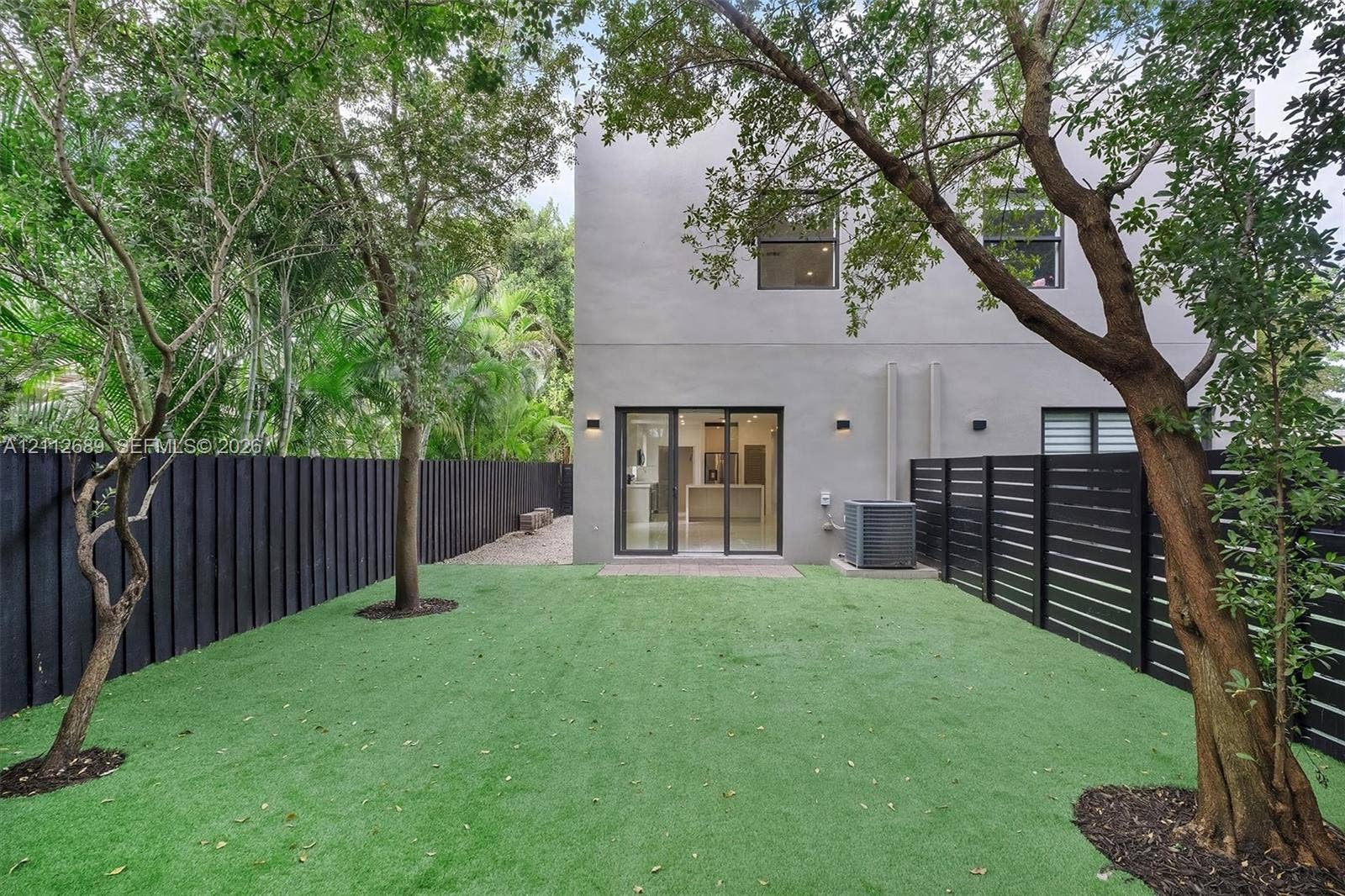 2889 SW 33rd Avenue, #2889, Miami, Miami, FL 33133 Fenced backyard featuring synthetic turf, mature trees, smooth stucco exterior, and sliding glass doors