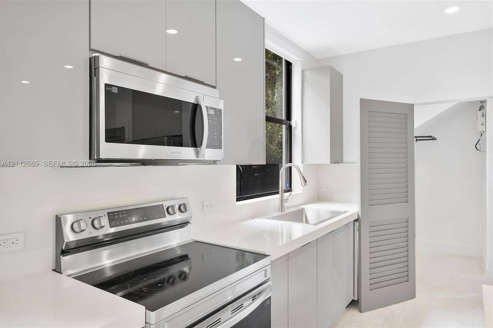 2889 SW 33rd Avenue, #2889, Miami, Miami, FL 33133 Kitchen featuring flat-panel gray cabinetry, stainless steel appliances, white solid-surface countertops, an undermount sink with a gooseneck faucet, and a louvered interior door