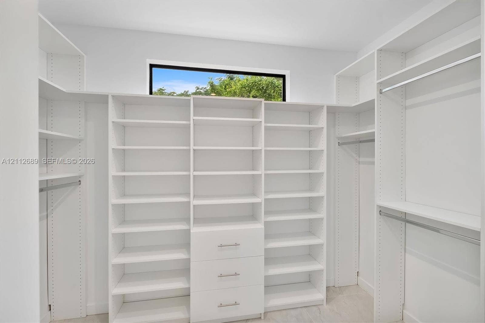 2889 SW 33rd Avenue, #2889, Miami, Miami, FL 33133 Walk-in closet featuring floor-to-ceiling white built-in shelving, integrated dresser drawers with metallic pulls, horizontal hanging rods, and a clerestory window