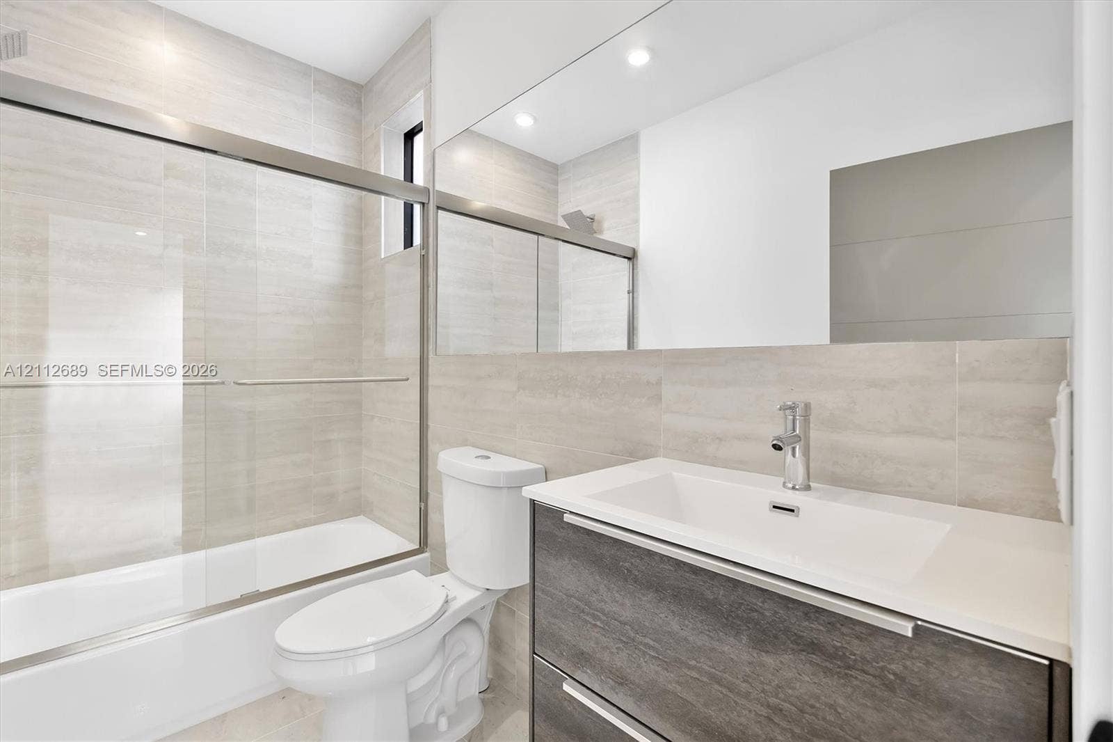 2889 SW 33rd Avenue, #2889, Miami, Miami, FL 33133 Bathroom featuring a wall-to-wall mirror, modern floating vanity with a stone-top integrated sink, floor-to-ceiling tile surround, and a glass-enclosed tub shower with metallic hardware