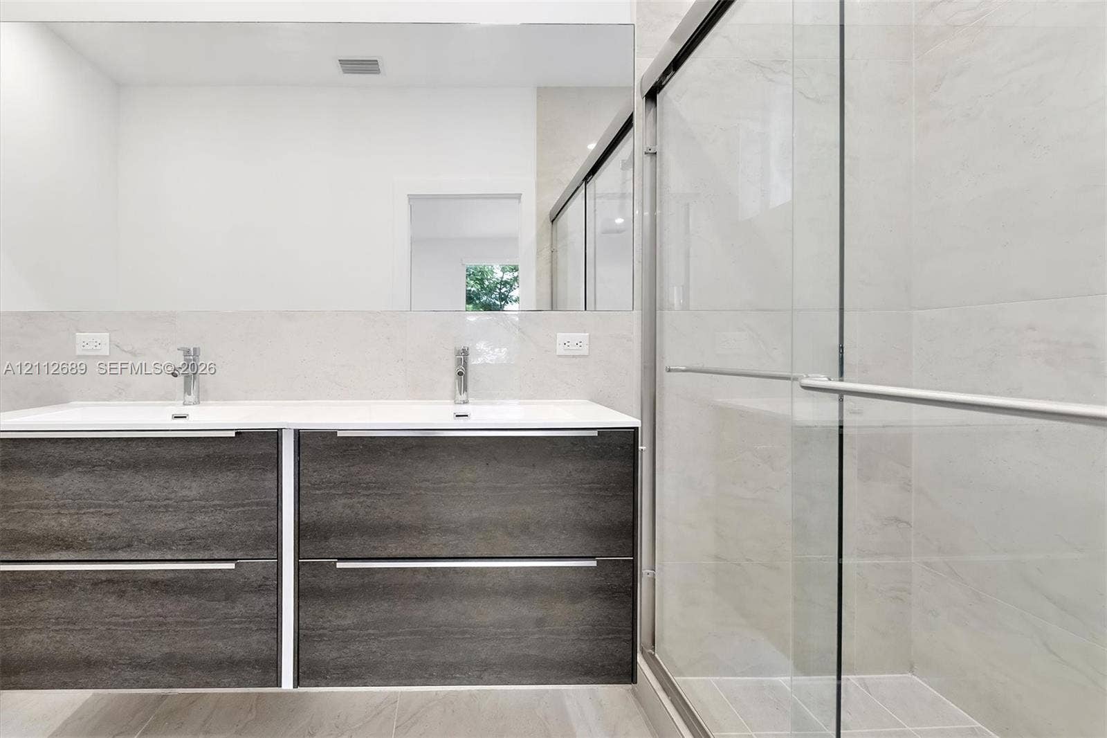 2889 SW 33rd Avenue, #2889, Miami, Miami, FL 33133 Floating wood-finish double vanity with dual undermount sinks and chrome fixtures, large wall-mounted mirror, and walk-in shower featuring glass sliding doors and floor-to-ceiling tile surround