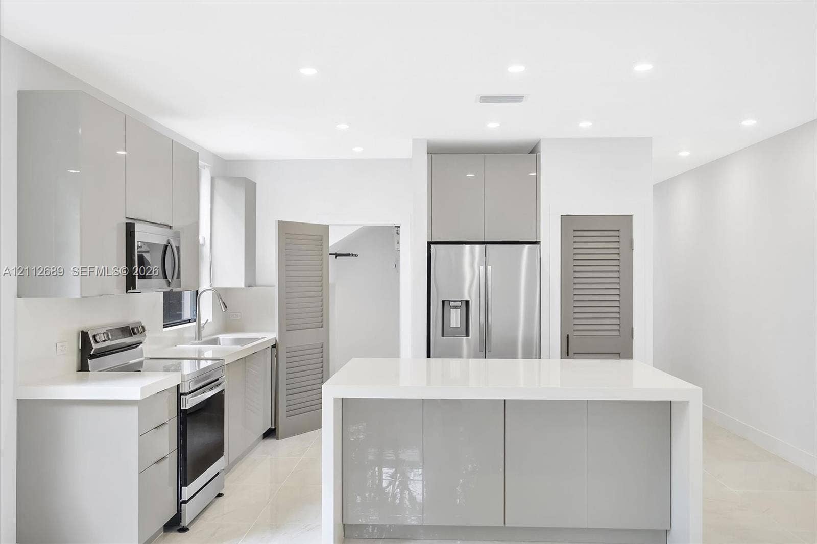 2889 SW 33rd Avenue, #2889, Miami, Miami, FL 33133 Contemporary kitchen featuring high-gloss cabinetry, a central island with a solid-surface countertop, stainless steel appliances, recessed ceiling lighting, and large-format tile flooring