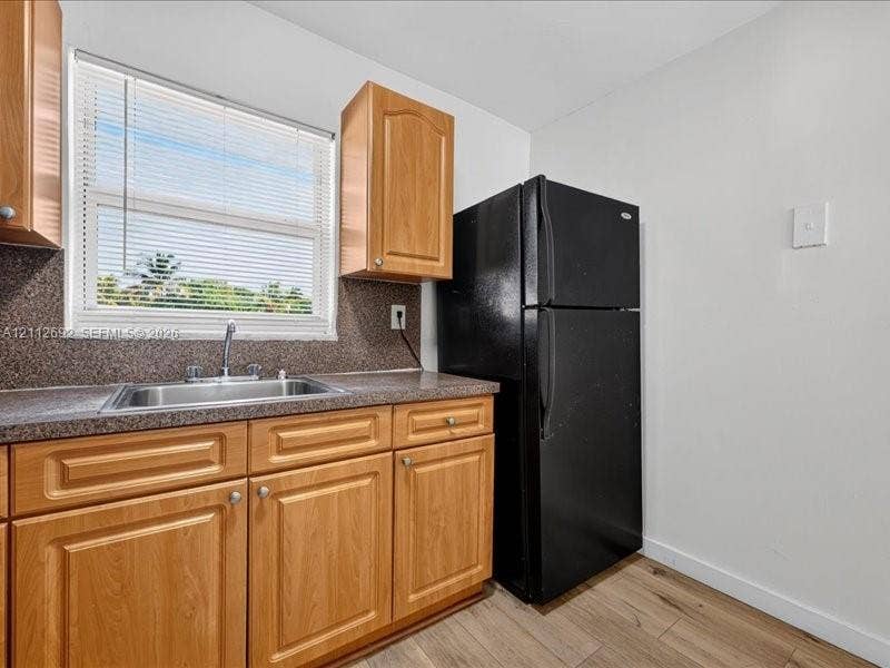 1111 NW 19th Avenue, #205, Miami, FL 33125 Kitchen featuring natural finish wood cabinetry, stone-textured countertop, stainless steel sink with a chrome faucet, black refrigerator, and wood-finish flooring