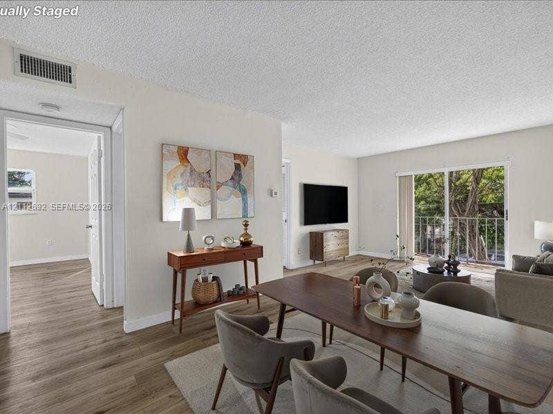 1111 NW 19th Avenue, #205, Miami, FL 33125 Open-concept interior featuring wood-finish flooring, sliding glass doors to a balcony, and white-painted walls