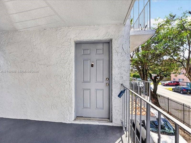 1111 NW 19th Avenue, #205, Miami, FL 33125 Exterior entry featuring a textured stucco facade, a paneled door with hardware, and a metal railed walkway