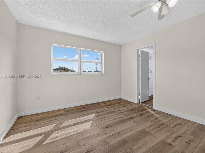 1111 NW 19th Avenue, #205, Miami, FL 33125 Neutral interior featuring wood-finish flooring, white walls, a dual-pane horizontal sliding window, and a white ceiling fan with integrated lighting