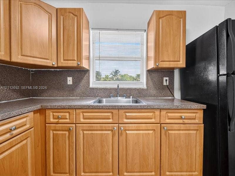 1111 NW 19th Avenue, #205, Miami, FL 33125 Kitchen featuring wood-finish cabinetry, speckled laminate countertops, a stainless steel sink with a dual-handle faucet, and an integrated black refrigerator