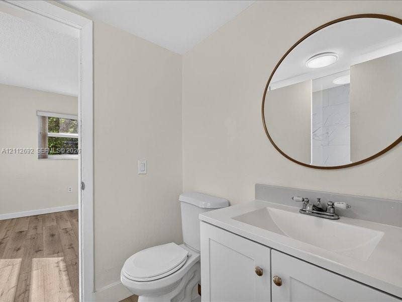 1111 NW 19th Avenue, #205, Miami, FL 33125 White vanity with a rectangular integrated sink, neutral stone-finish backsplash, oval mirror with a metallic frame, and a dual-handle faucet