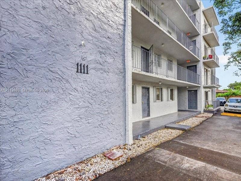 1111 NW 19th Avenue, #205, Miami, FL 33125 Multi-level building exterior featuring textured stucco siding, stacked balconies with metal railings, and a gravel border
