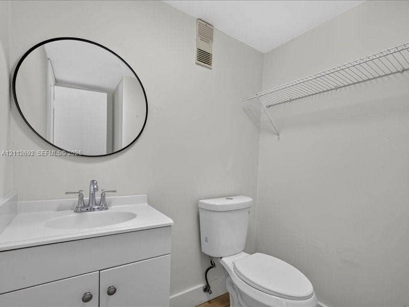 1111 NW 19th Avenue, #205, Miami, FL 33125 White vanity with an integrated countertop, oval mirror featuring a matte black frame, dual-handle faucet, and white wall-mounted wire shelving