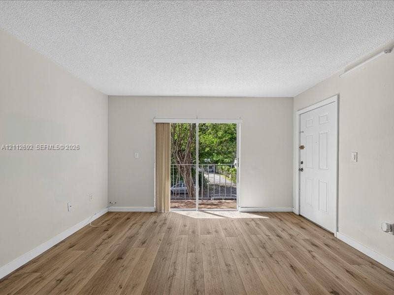 1111 NW 19th Avenue, #205, Miami, FL 33125 Living area featuring wood-finish flooring, neutral wall paint, and sliding glass doors with access to an exterior balcony
