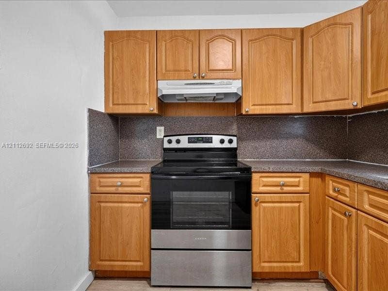 1111 NW 19th Avenue, #205, Miami, FL 33125 Kitchen featuring arched-panel wood cabinetry, stone-composite countertops, and an integrated stainless-steel range with a matching overhead hood