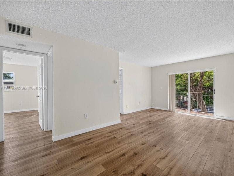 1111 NW 19th Avenue, #205, Miami, FL 33125 Open-concept interior featuring wood-finish flooring, neutral wall paint, and sliding glass doors with exterior railing