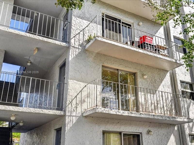 1111 NW 19th Avenue, #205, Miami, FL 33125 Multi-story exterior featuring a textured stucco facade, stacked private balconies with metal railings, and sliding glass door entries