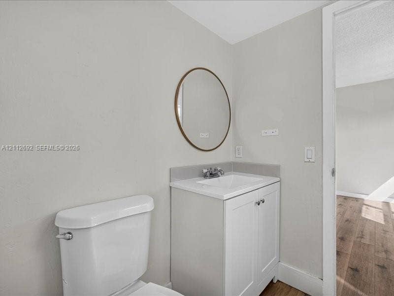 1111 NW 19th Avenue, #205, Miami, FL 33125 White vanity with integrated basin, chrome-finish dual-handle faucet, oval-shaped wall-mounted mirror with bronze-toned frame, and white porcelain toilet