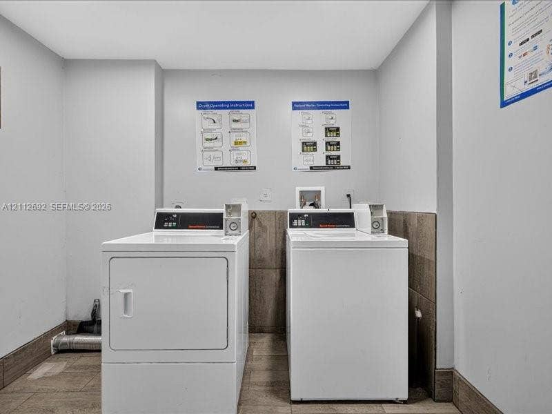 1111 NW 19th Avenue, #205, Miami, FL 33125 Laundry area featuring dual top-loading washer and front-loading dryer units, tile flooring, and half-height wall tiling