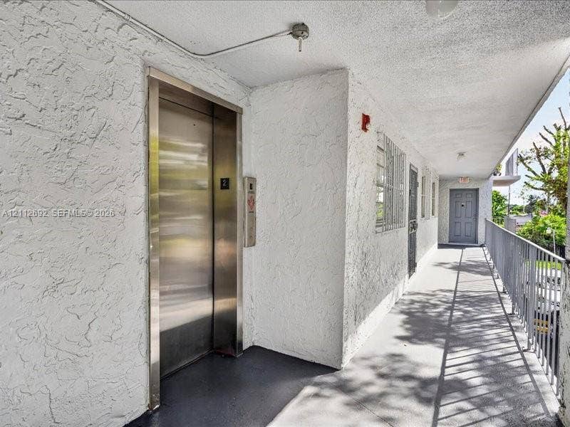 1111 NW 19th Avenue, #205, Miami, FL 33125 Exterior walkway featuring a brushed-metal elevator door, textured stucco wall finishes, and a metal-railing enclosure