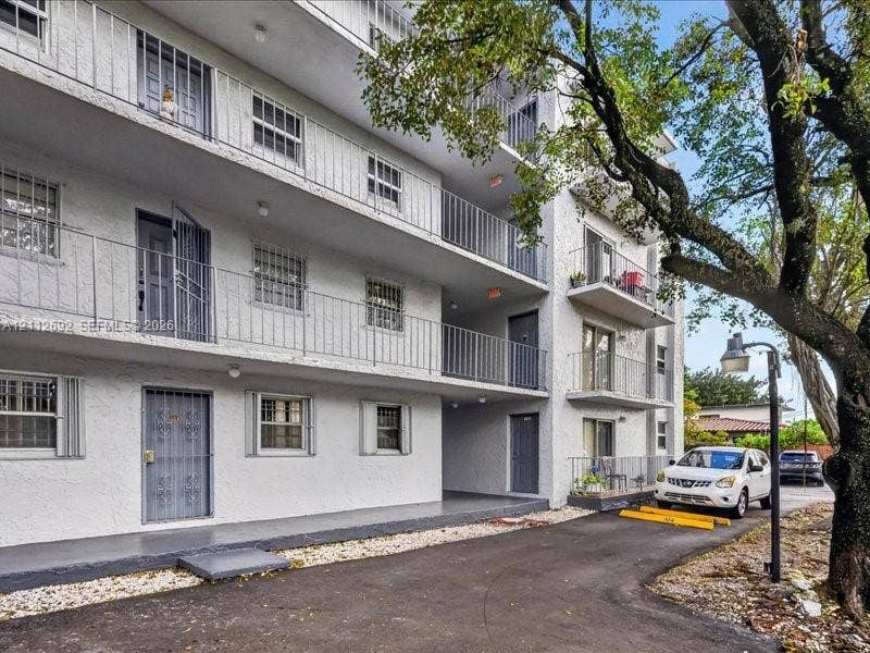 1111 NW 19th Avenue, #205, Miami, FL 33125 Multi-story structure with a textured stucco facade, tiered exterior balcony walkways, metal railings, and dedicated asphalt parking