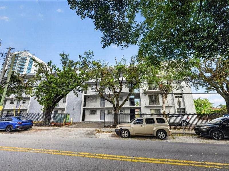 1111 NW 19th Avenue, #205, Miami, FL 33125 Multi-story residential building exterior featuring a light-toned stucco facade, private balconies, and perimeter metal fencing