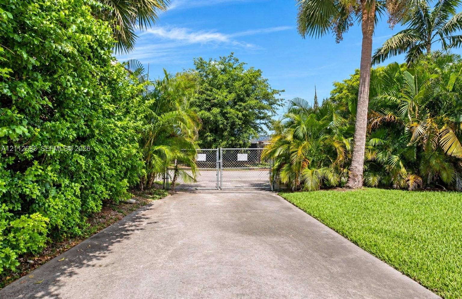 Homestead, Homestead, FL 33033 Concrete driveway leading to a gated entry, flanked by mature landscaping, palm trees, and a manicured lawn