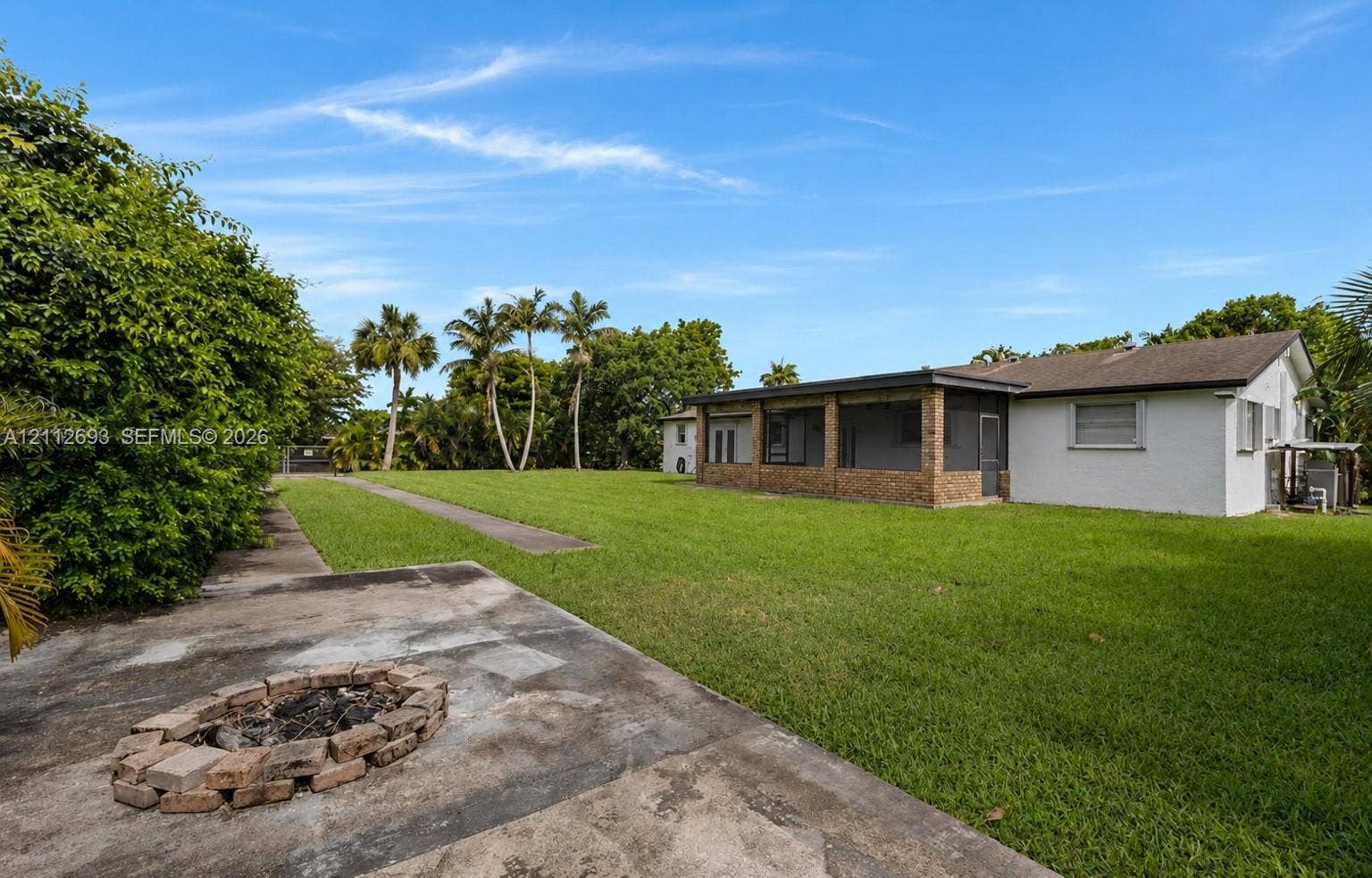 Homestead, Homestead, FL 33033 Expansive backyard featuring a sprawling lawn, a stone-accented screened-in patio, and a dedicated circular brick fire pit area