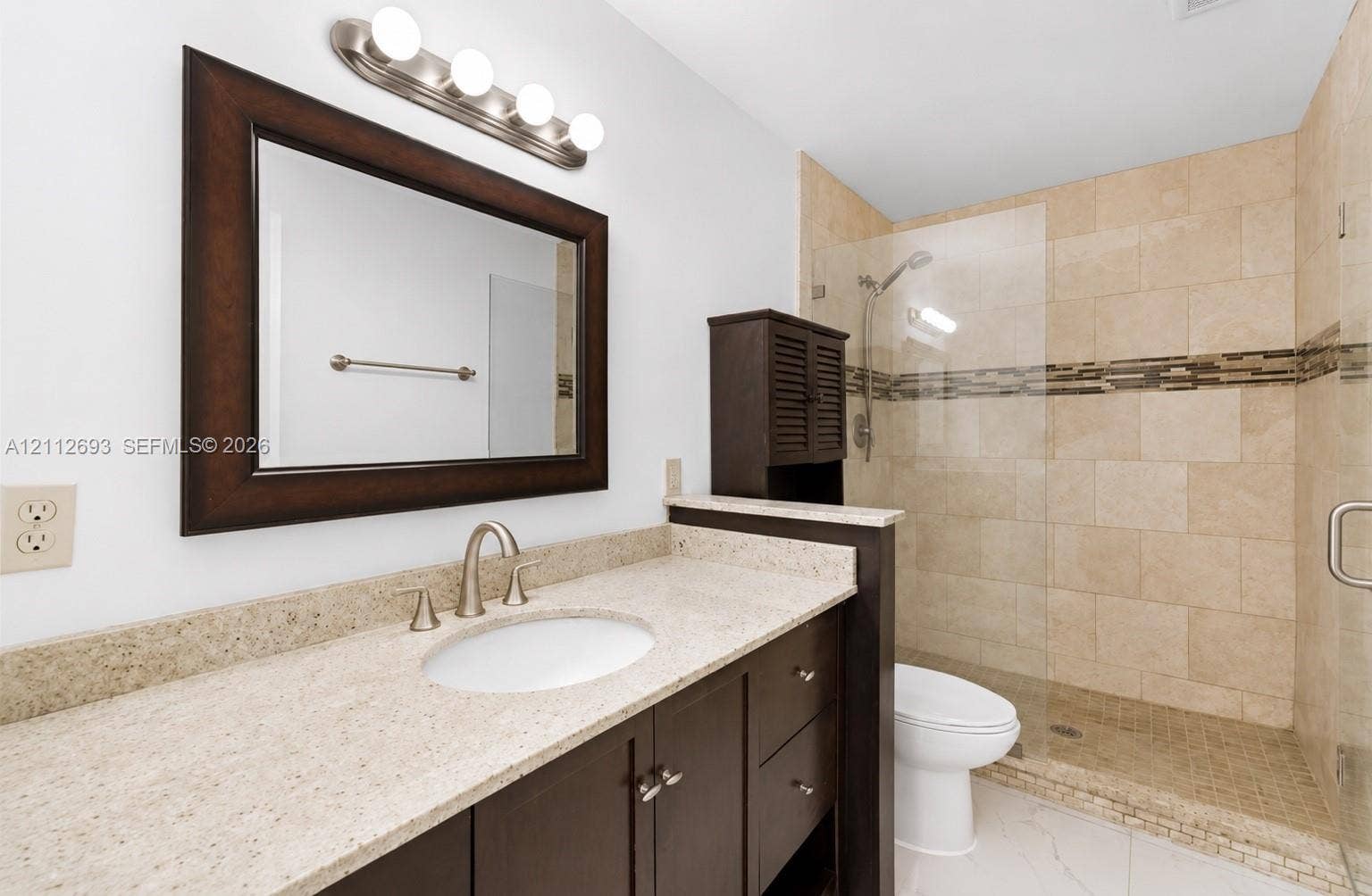 Homestead, Homestead, FL 33033 Bathroom featuring a dark-finish wood vanity with a stone countertop, an integrated oval sink, a glass-enclosed walk-in shower with stone tile surround, and a coordinating vanity mirror with an attached four-light fixture