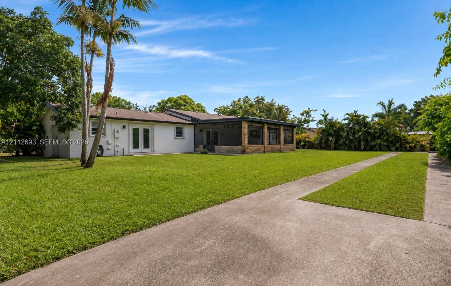 Homestead, Homestead, FL 33033 Expansive backyard featuring a sprawling lawn, mature palm trees, a concrete driveway, and a covered patio area with masonry detailing