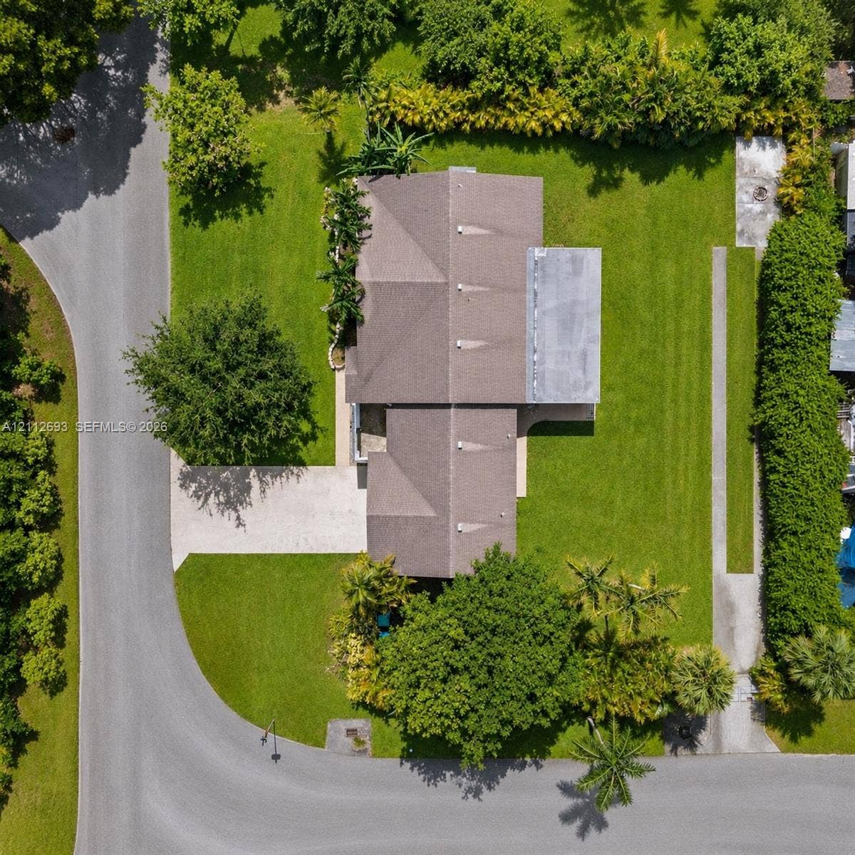 Homestead, Homestead, FL 33033 Aerial perspective featuring a multi-hipped roofline, expansive grass lawn, paved driveway, mature trees, and dense perimeter landscaping