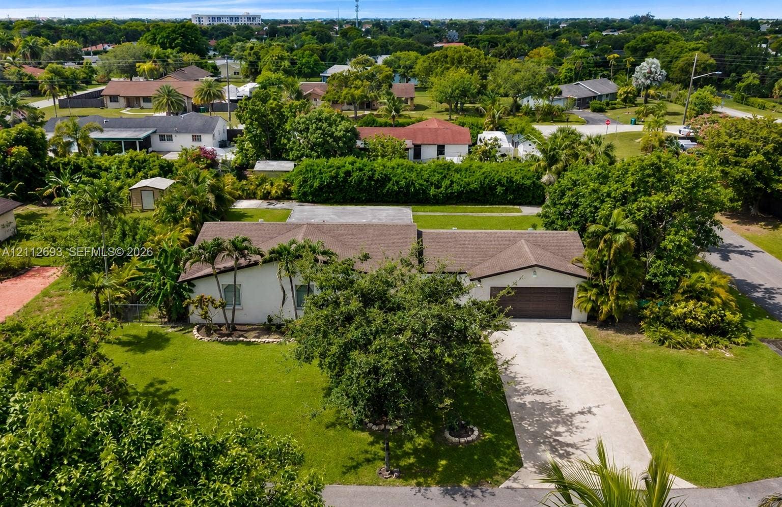 Homestead, Homestead, FL 33033 Single-story residence featuring a shingled roof, stucco exterior, attached two-car garage, concrete driveway, and expansive lot with mature landscaping