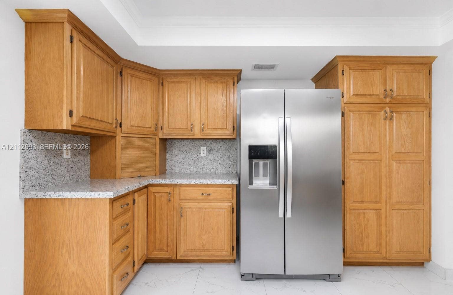 Homestead, Homestead, FL 33033 Kitchen featuring natural wood cabinetry, light-toned speckled stone countertops, and a side-by-side stainless steel refrigerator with an integrated water and ice dispenser