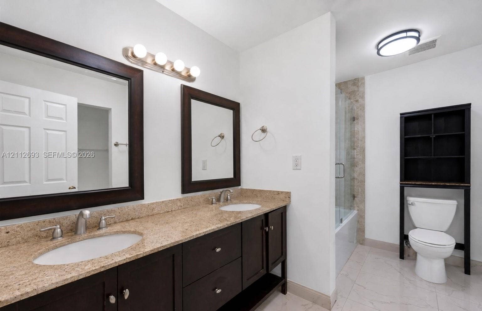 Homestead, Homestead, FL 33033 Dual-sink vanity with stone countertop, dark cabinetry, framed mirrors, and a glass-enclosed shower featuring tile surrounds