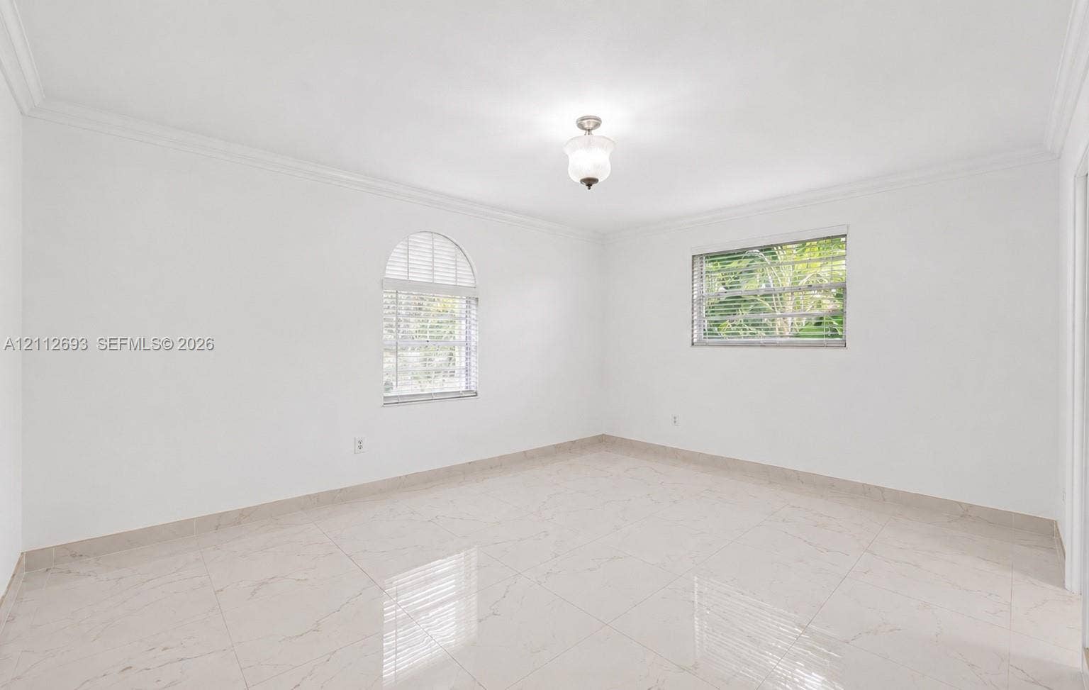 Homestead, Homestead, FL 33033 Neutral-toned interior space featuring polished tile flooring, crown molding, an arched window, and a centered flush-mount light fixture