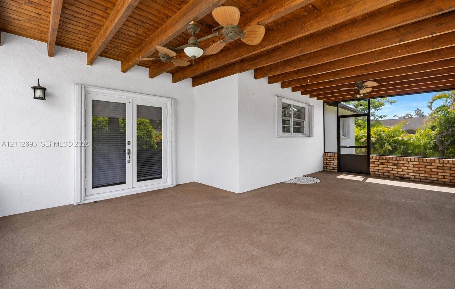 Homestead, Homestead, FL 33033 Covered patio featuring exposed wood-beam ceiling, dual ceiling fans, white stucco walls, French door entry, and screened enclosure with brick-accented base