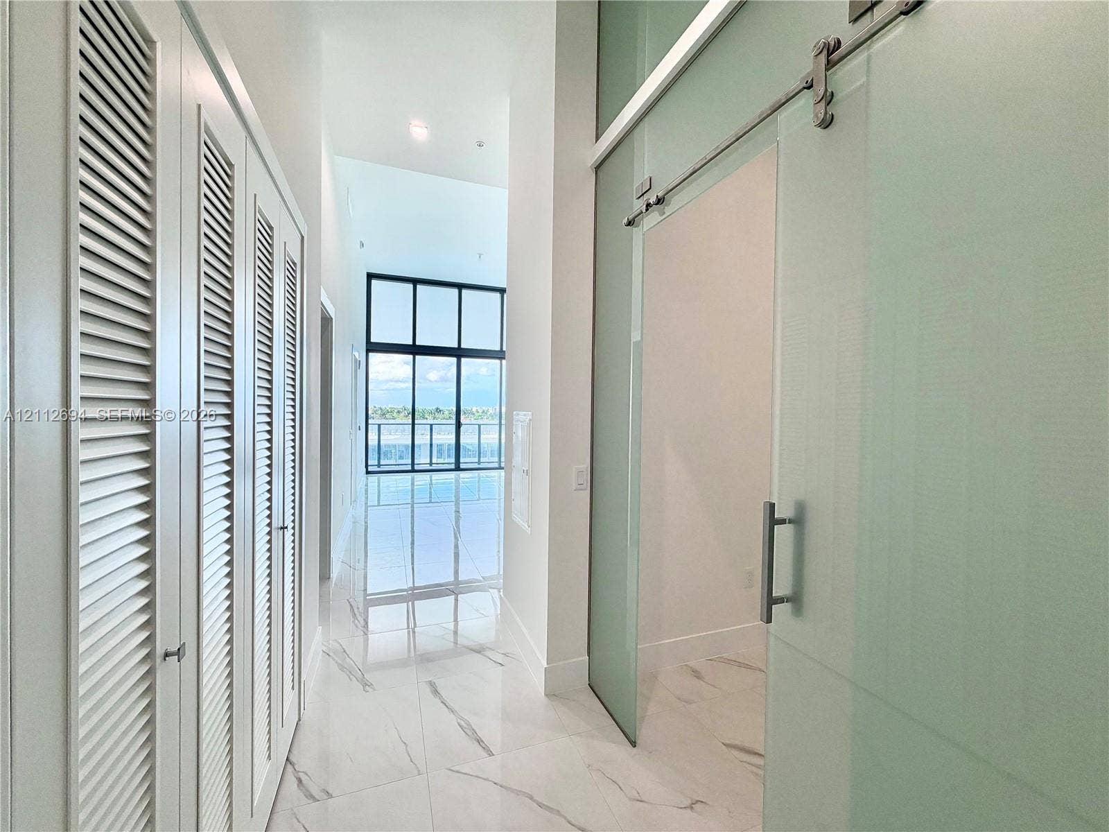 1170 E Hallandale Beach Boulevard, #503, Hallandale Beach, Hallandale Beach, FL 33009 Hallway featuring large-format stone-finish flooring, floor-to-ceiling louvered cabinetry, and a sliding glass door with a polished metal track system
