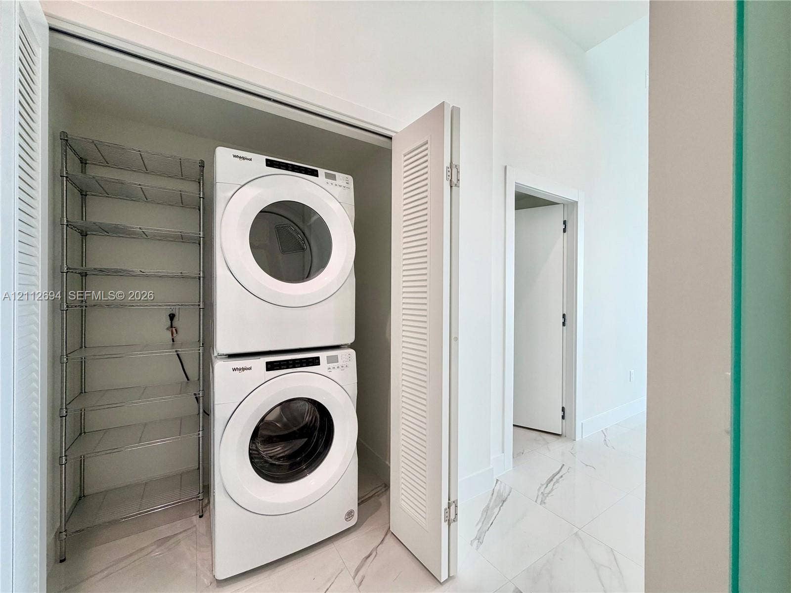 1170 E Hallandale Beach Boulevard, #503, Hallandale Beach, Hallandale Beach, FL 33009 Laundry closet featuring louvered bifold doors, stone-finish tile flooring, and integrated metal shelving