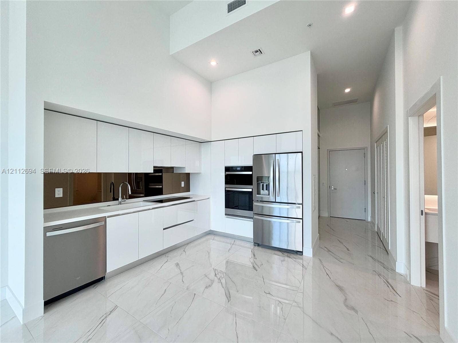 1170 E Hallandale Beach Boulevard, #503, Hallandale Beach, Hallandale Beach, FL 33009 High-gloss white cabinetry, polished stone-finish flooring with veining, stainless steel built-in appliances, a mirrored backsplash, and high ceilings