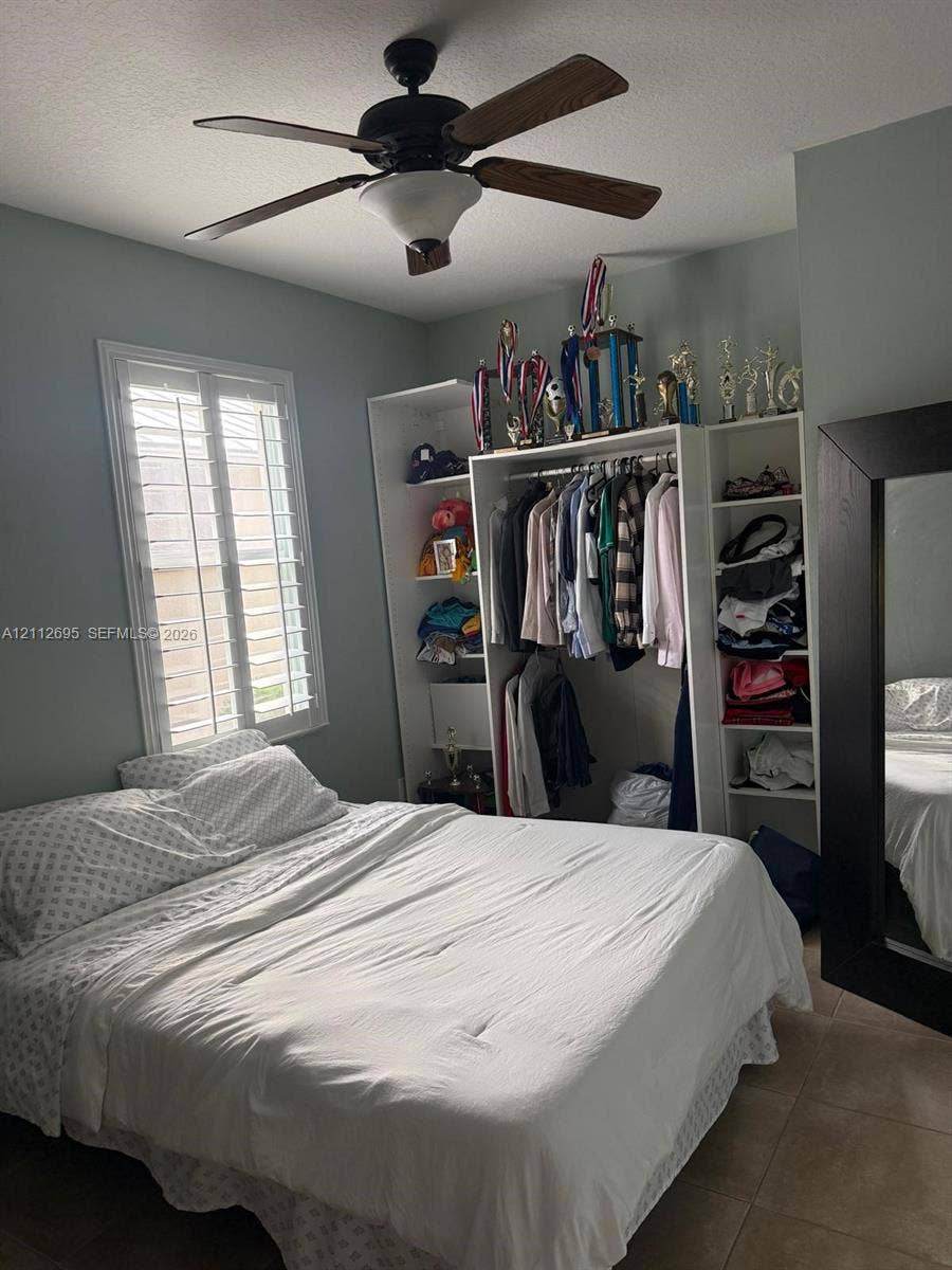 9812 SW Glenbrook Drive, Port St Lucie, FL 34987 Room featuring white plantation shutters, a multi-blade ceiling fan, and built-in closet cabinetry