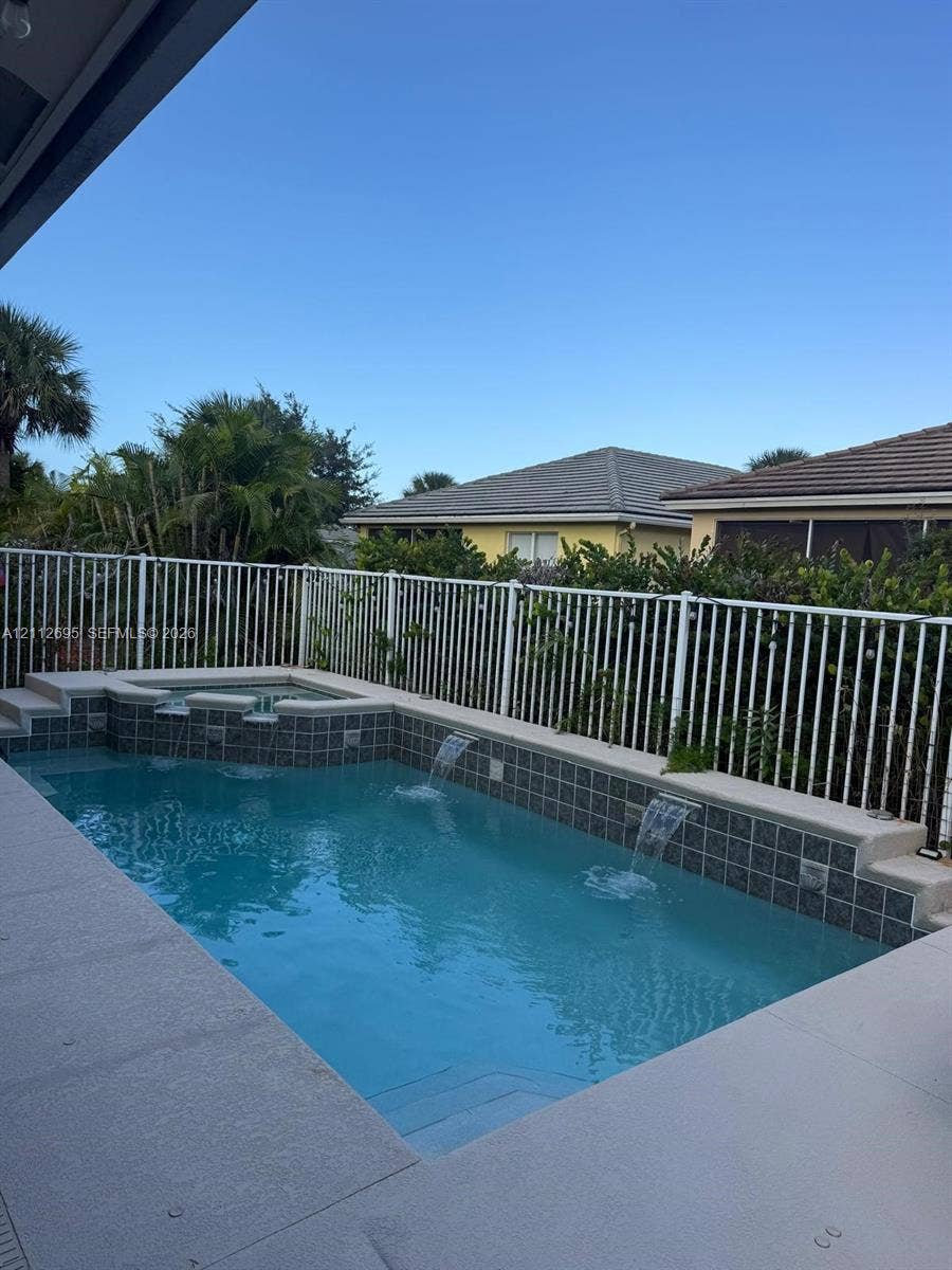9812 SW Glenbrook Drive, Port St Lucie, FL 34987 In-ground pool featuring a tiled waterline, integrated spillway spa, dual water features, and a concrete deck enclosed by metal fencing
