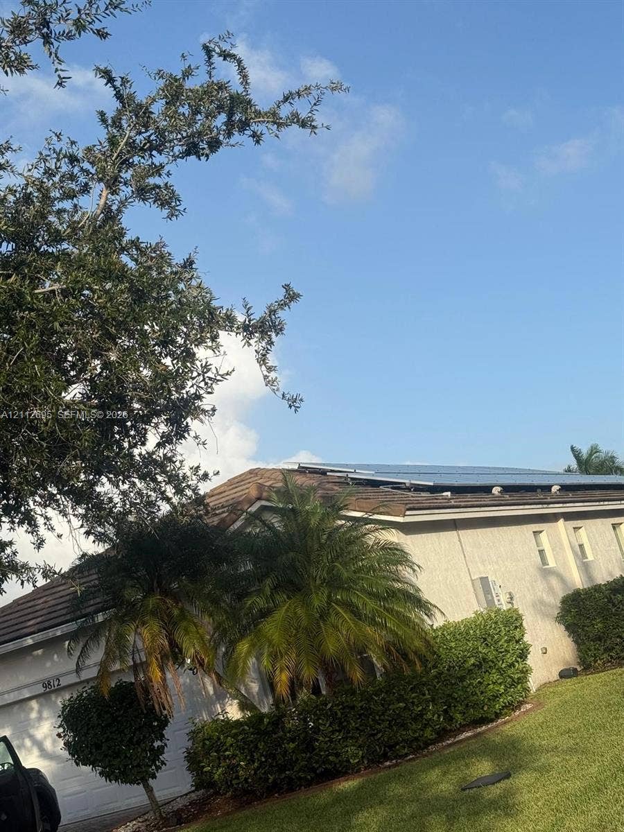9812 SW Glenbrook Drive, Port St Lucie, FL 34987 Exterior featuring a tiled roof with integrated solar panels, stucco siding, and mature landscaping