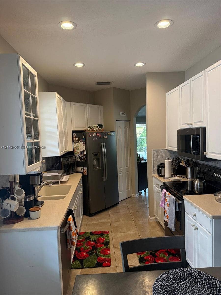 9812 SW Glenbrook Drive, Port St Lucie, FL 34987 Kitchen featuring white shaker-style cabinetry, solid-surface countertops, recessed lighting, tile flooring, and glass-front upper cabinet doors