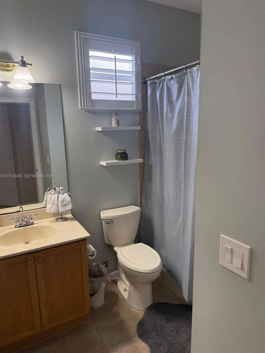 9812 SW Glenbrook Drive, Port St Lucie, FL 34987 Bathroom featuring a vanity with a neutral-toned integrated sink, wall-mounted white shelving, a window with plantation-style shutters, and a combined tub and shower unit