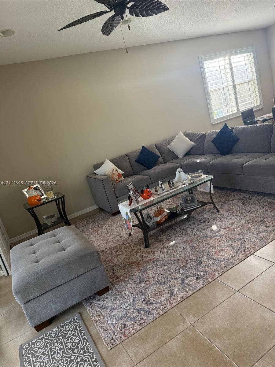 9812 SW Glenbrook Drive, Port St Lucie, FL 34987 Neutral wall palette featuring large-format tile flooring, plantation shutters, and a ceiling-mounted fan with integrated lighting